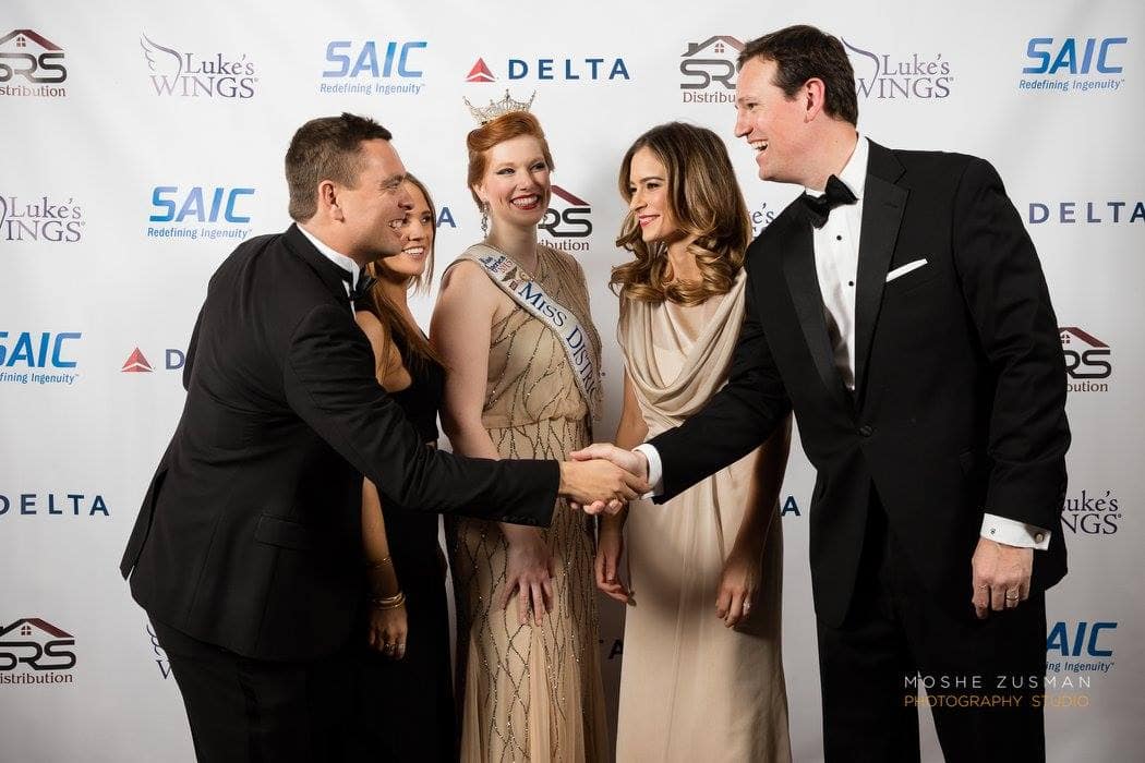 Five people dressed elegantly at a formal event, shaking hands and smiling.