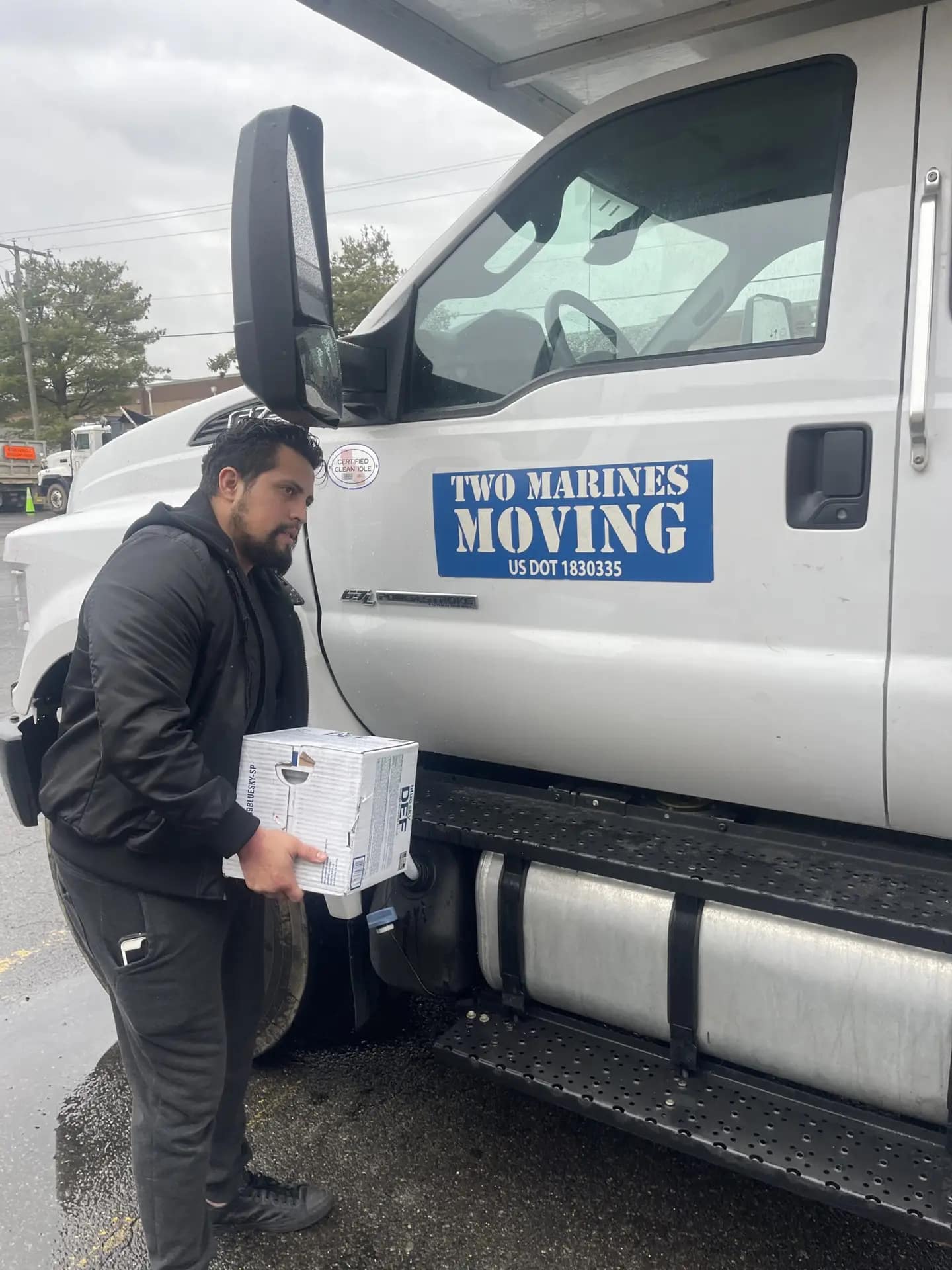 A man carrying a box near a moving truck labeled "The Movers Moving."