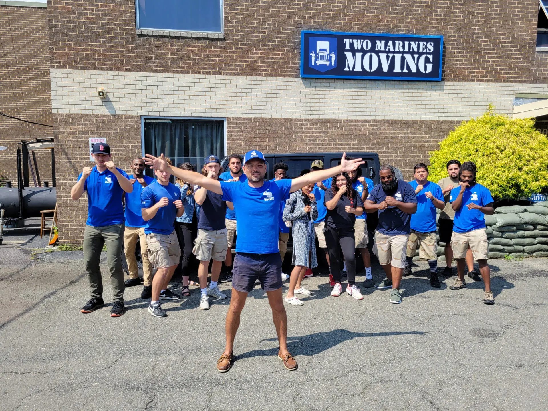 Team celebrating outside Two Marines Moving location in matching blue shirts.