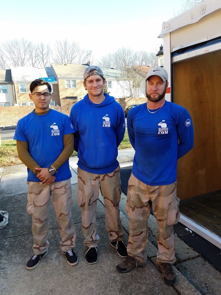 Three men in blue shirts and camouflage pants standing outdoors.